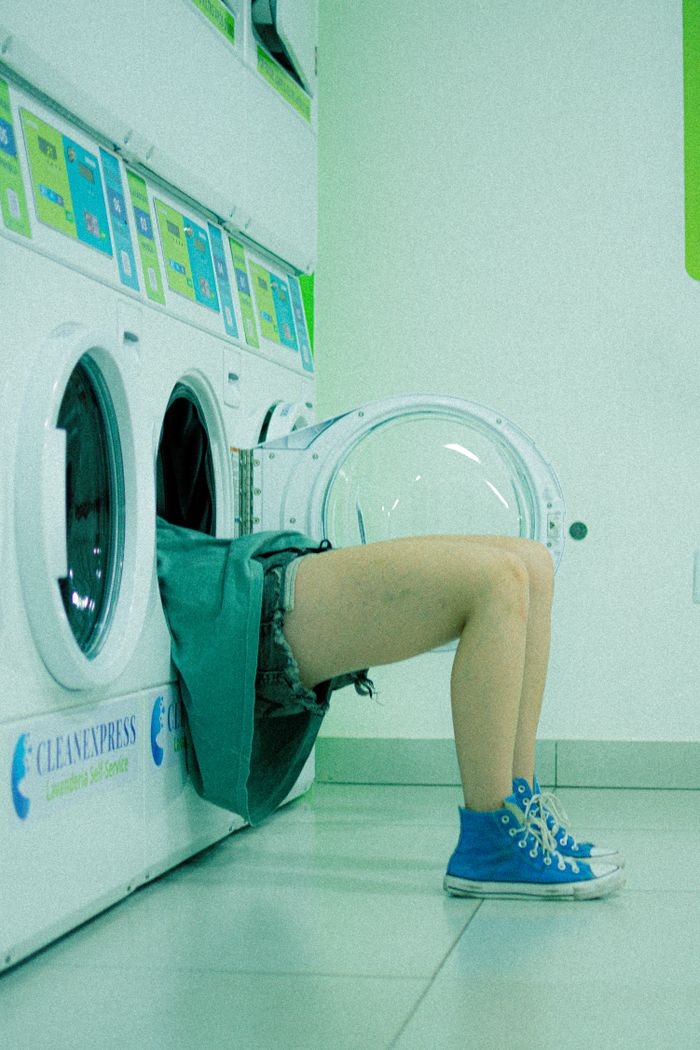 who-we-are Humorous image of a person partially inside a washing machine at a laundromat.